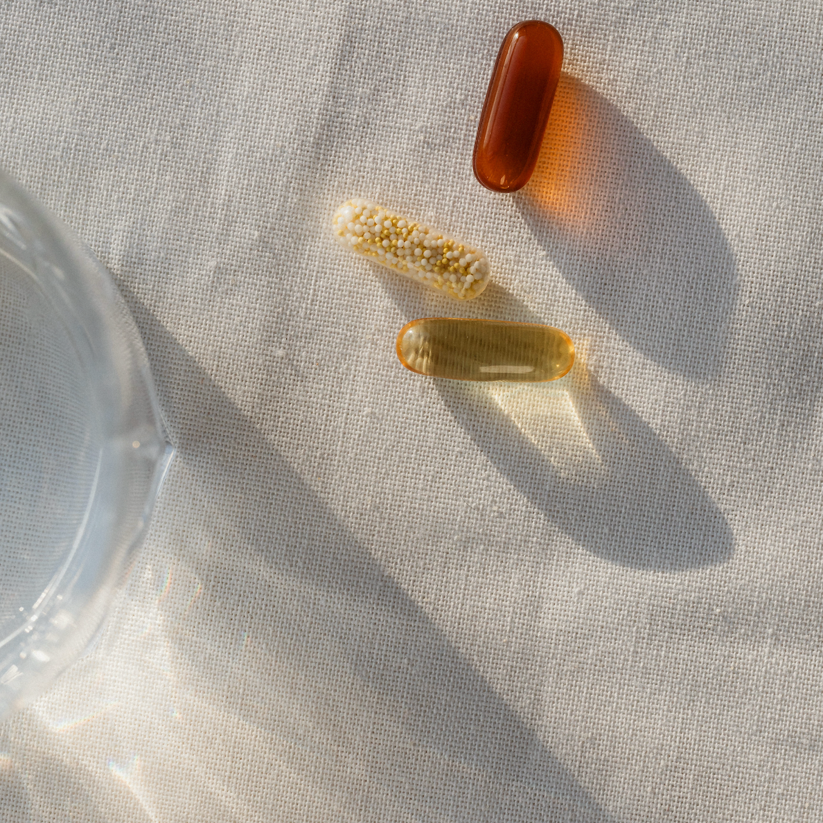 Three dietary supplement capsules (omega-3, herbal, and multivitamin) on a linen surface in natural sunlight, representing natural menopause support.