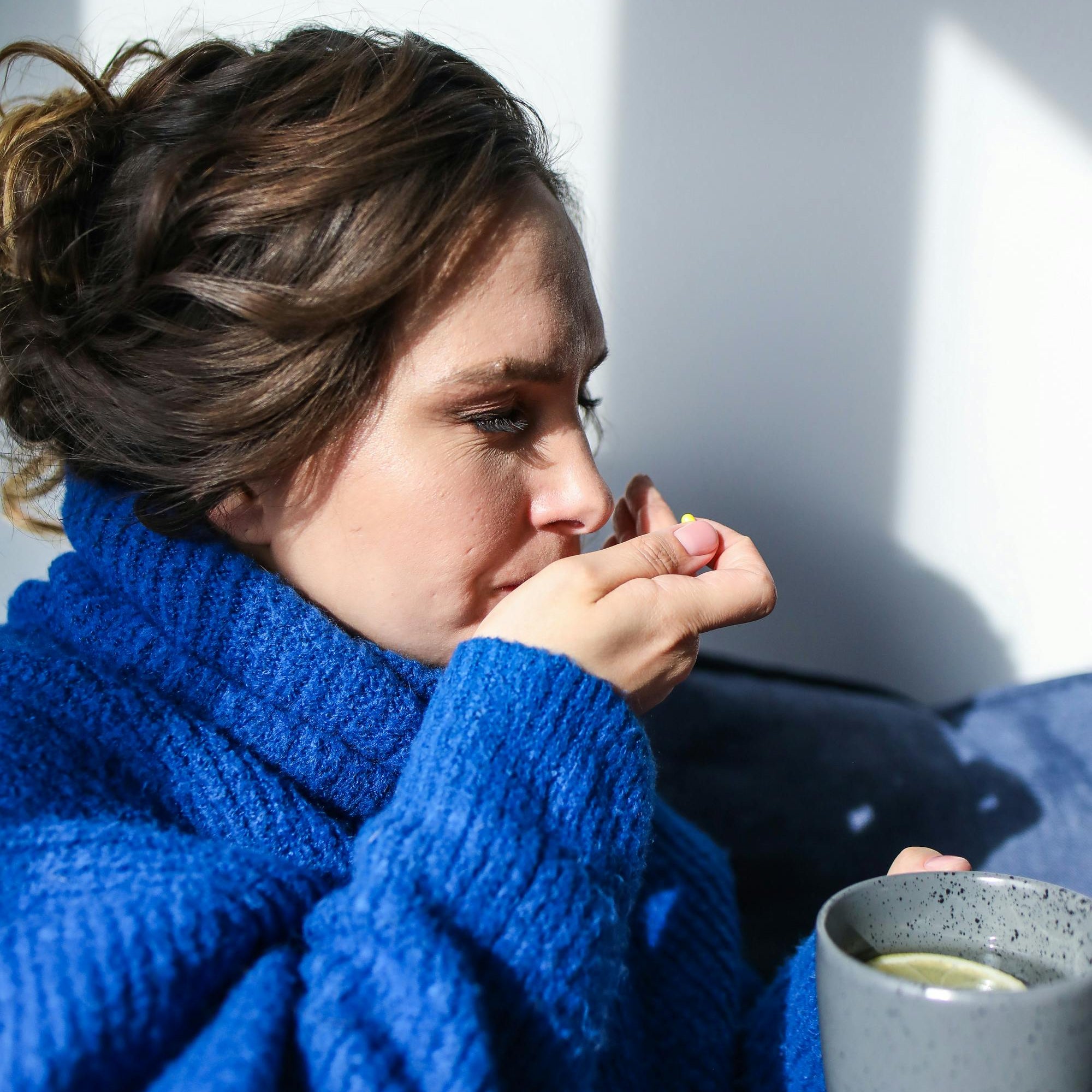 Woman holding a warm drink and taking a supplement capsule