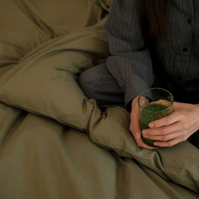Fatigued woman starting her day in bed with a comforting cup of supplements to support energy and balance.