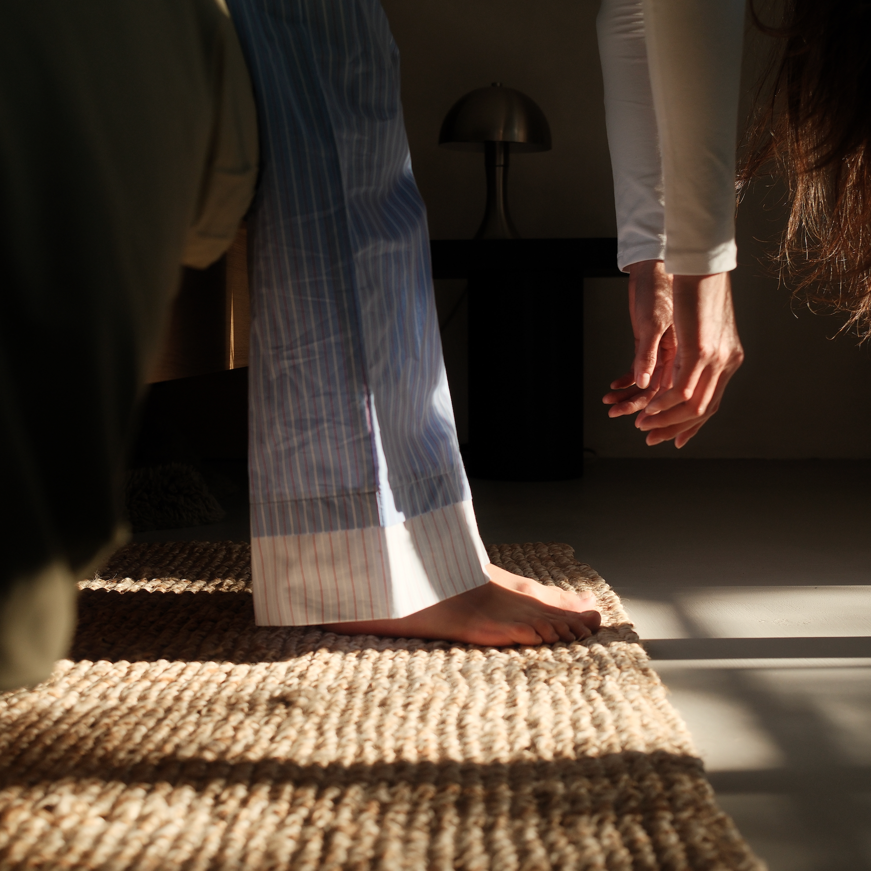 A woman gently stretching on a woven rug in morning light, symbolising self-care and natural wellness practices for menopause support.