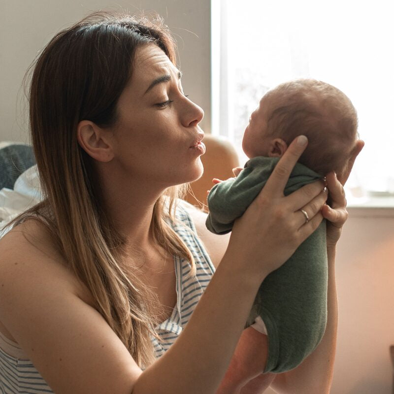 Mother sitting by a window holding her newborn baby in the early postnatal period