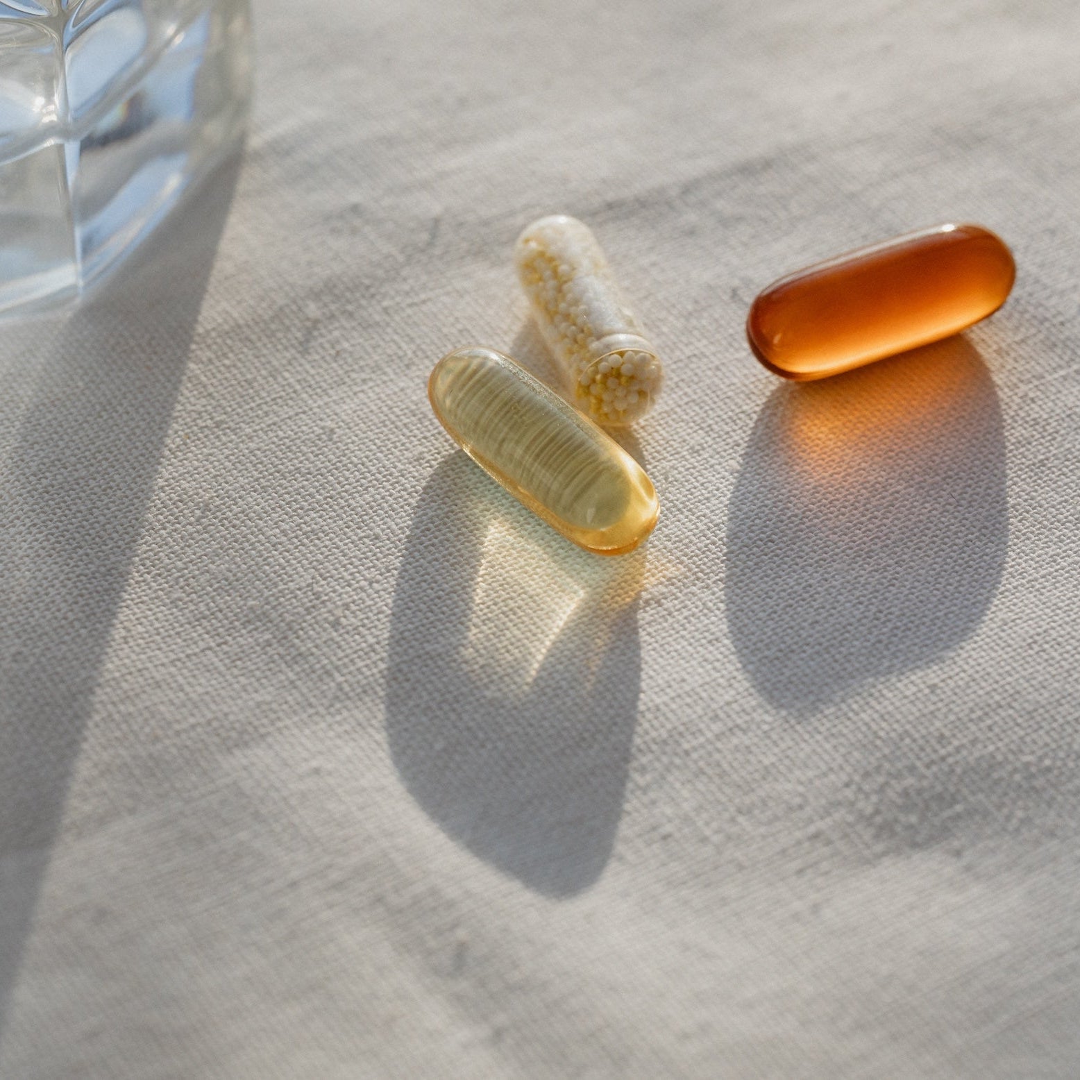 Three natural supplement capsules on fabric in soft morning light, symbolising daily wellness support.