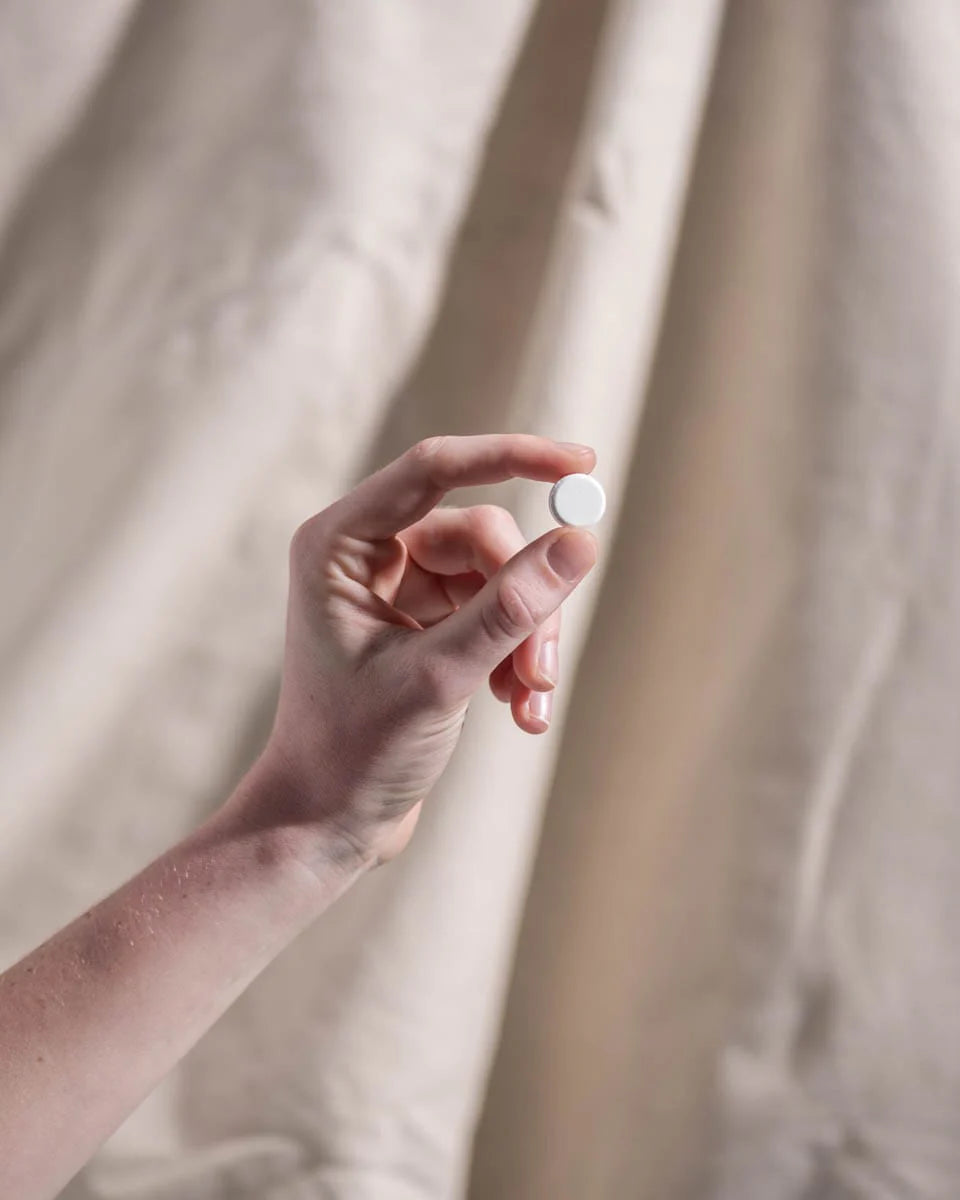 Child’s hand holding a Herbs of Gold Children’s Magnesium Care bottle while peeking through a light curtain.