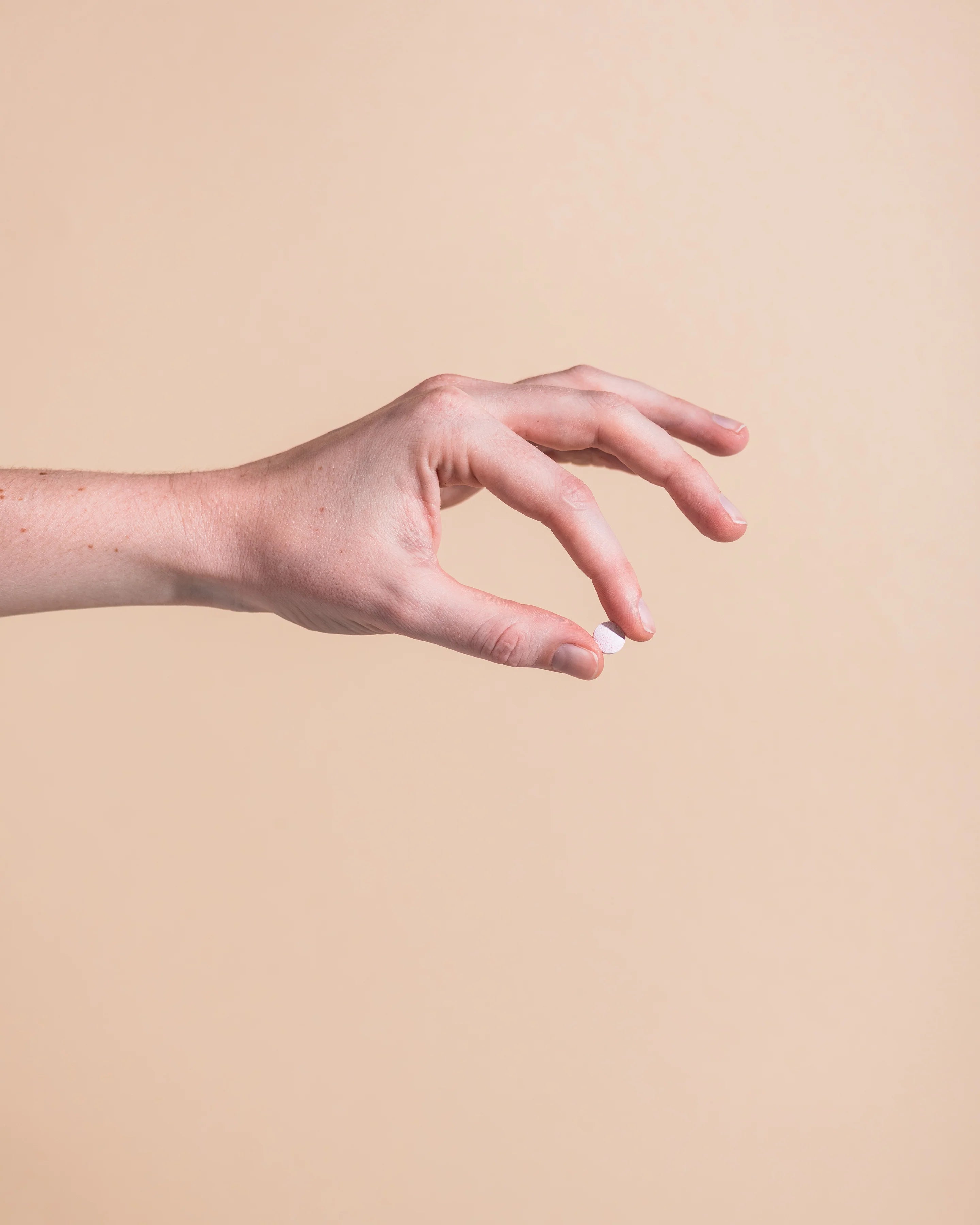 Close-up of a hand reaching toward a Herbs of Gold Activated Sublingual B12 bottle against a neutral beige background.