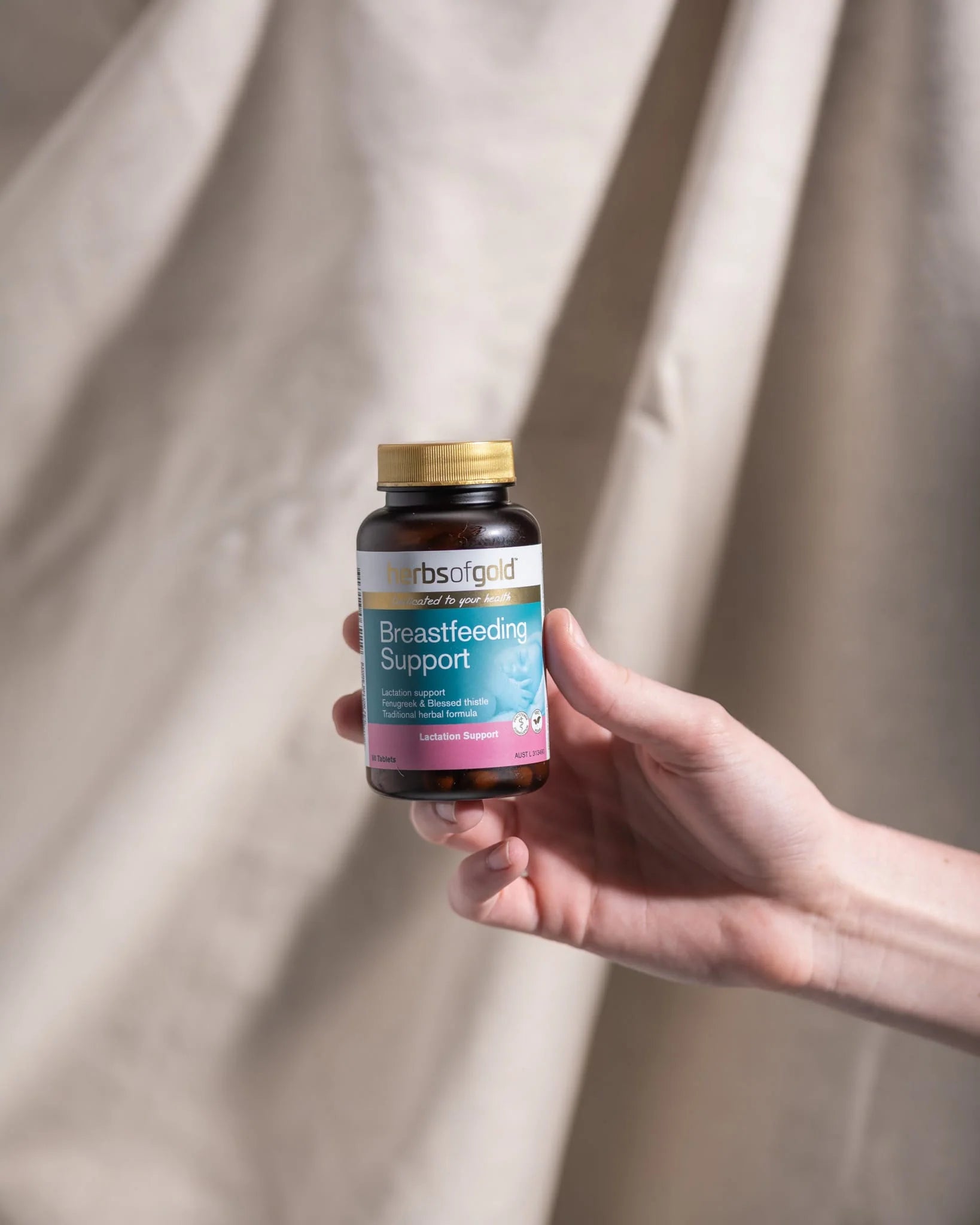 A hand holding a bottle of Herbs of Gold Breastfeeding Support