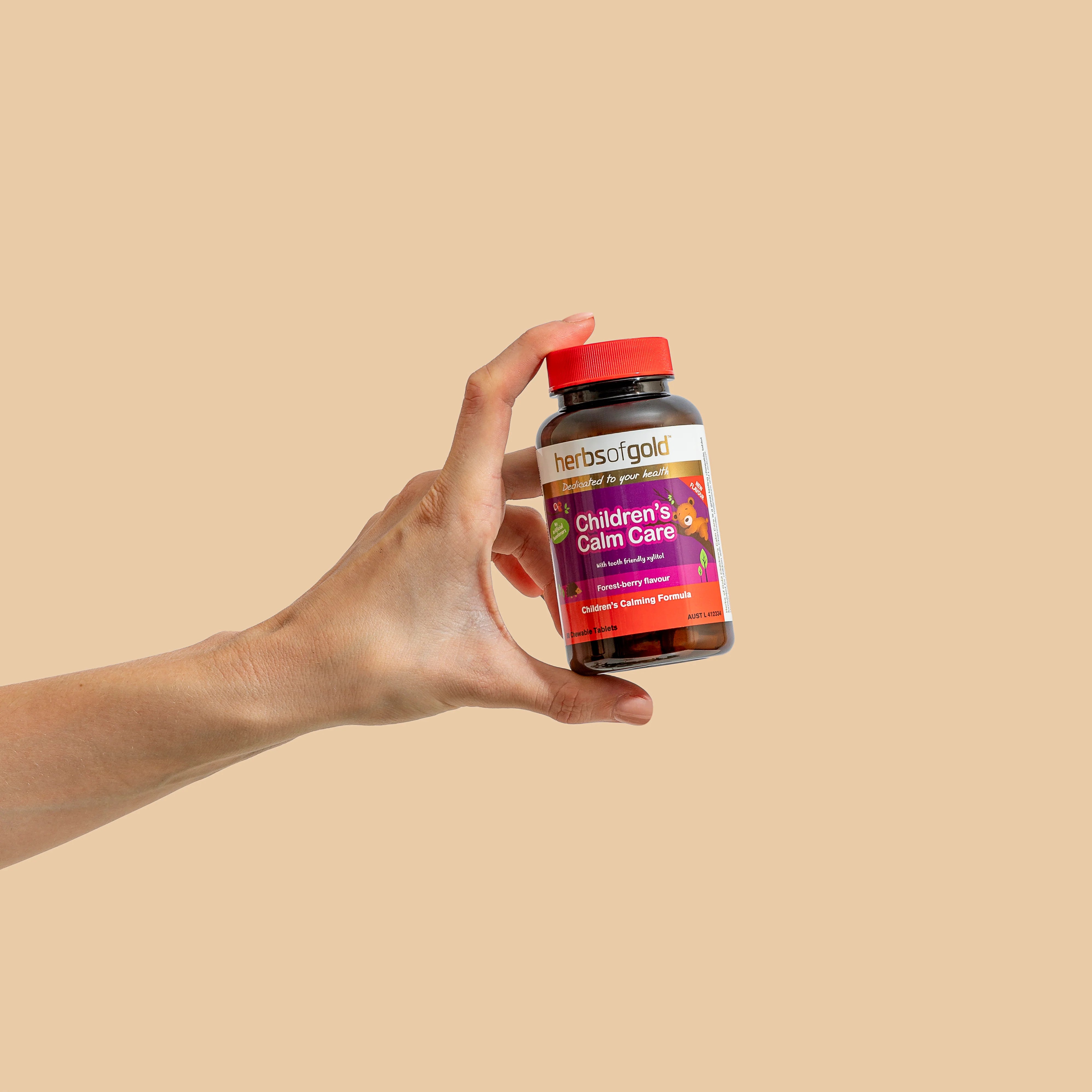 Hand holding a Herbs of Gold Children’s Calm Care bottle upright against a beige background.