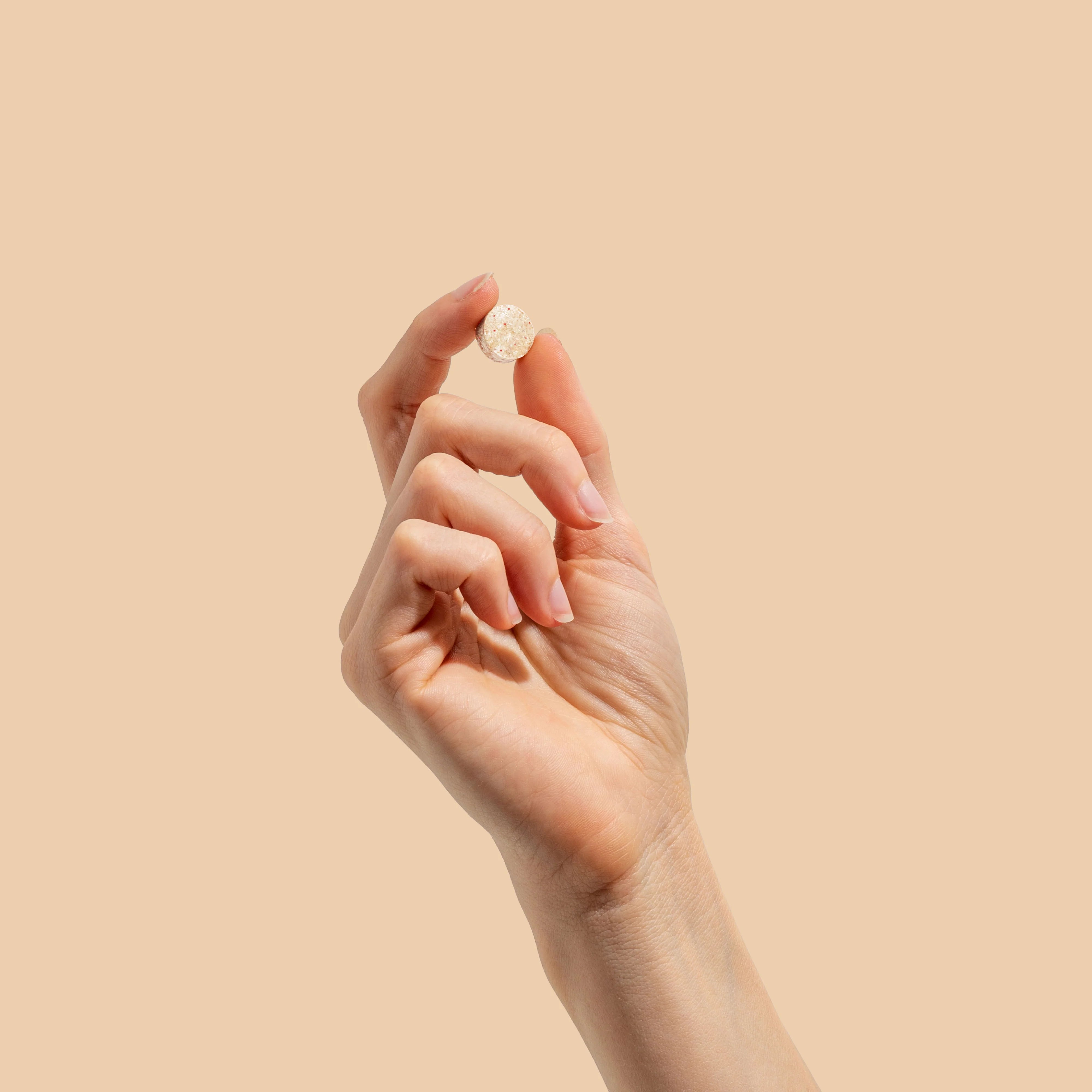 Hand holding a single Herbs of Gold Children’s Immune Care chewable tablet against a beige background.