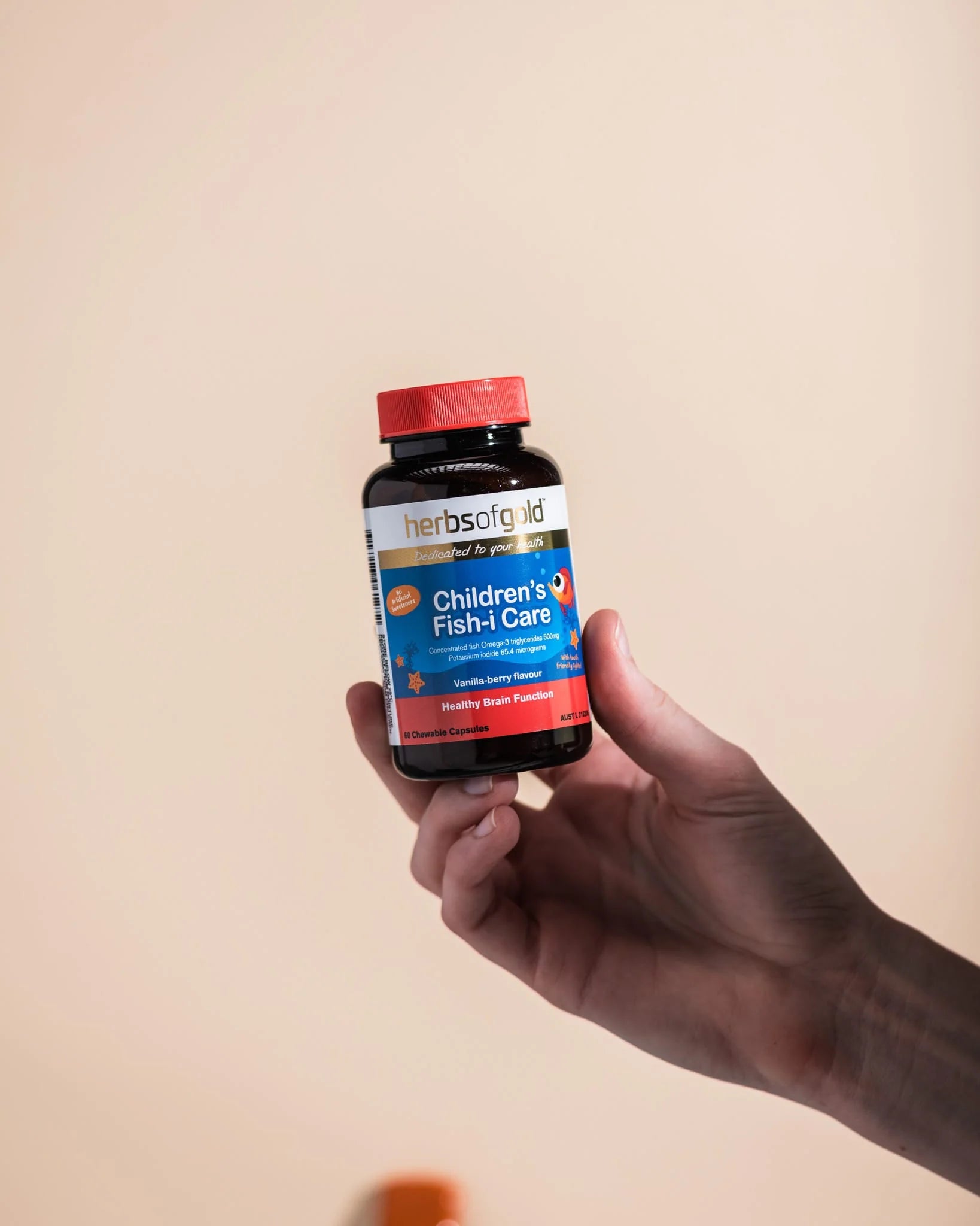 Hand holding a Herbs of Gold Children’s Fish-i Care bottle upright against a beige background.