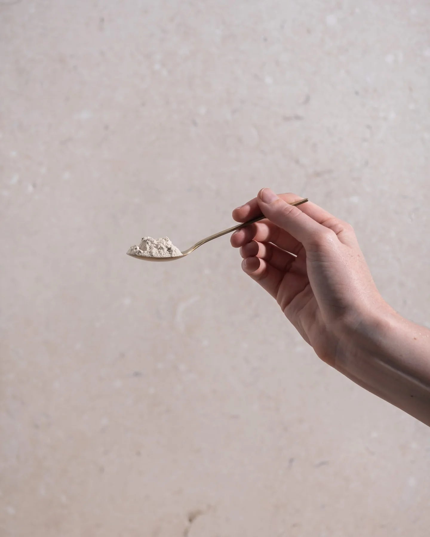 Hand holding a spoon with a scoop of white powder against a neutral background