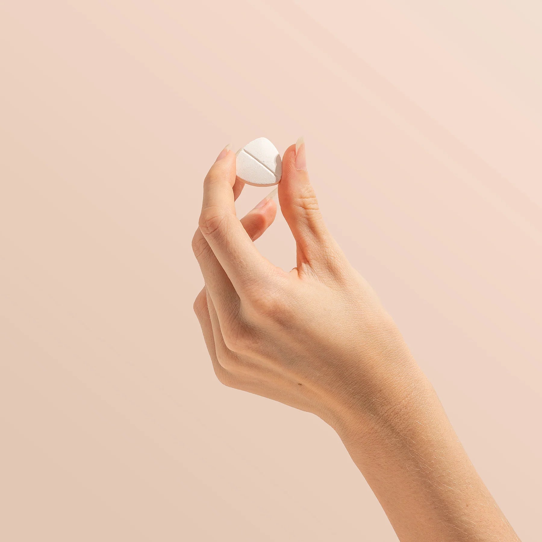 Hand holding a white pill against a beige background