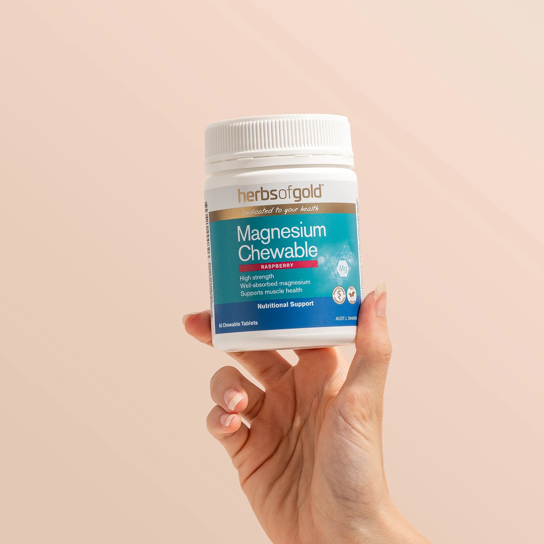 Hand holding a bottle of Herbs of Gold Magnesium Chewable on a beige background