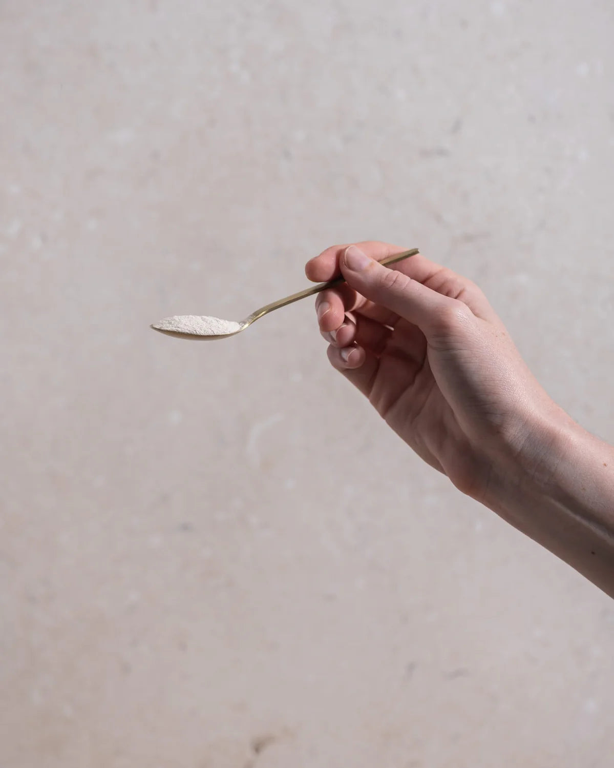 Hand holding a spoon with a white powdery substance against a neutral background
