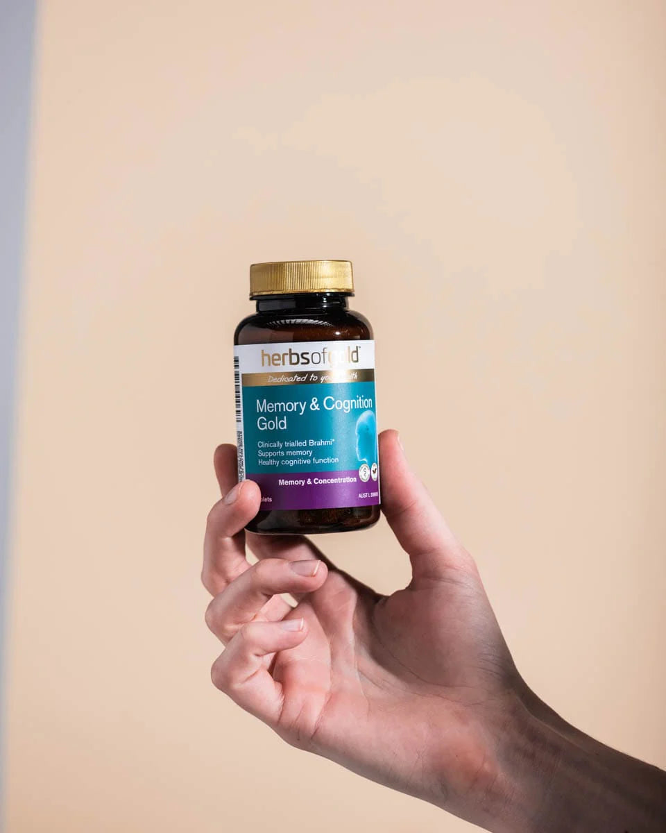 Hand holding a bottle of 'Memory & Cognitive Gold' supplement against a plain background.