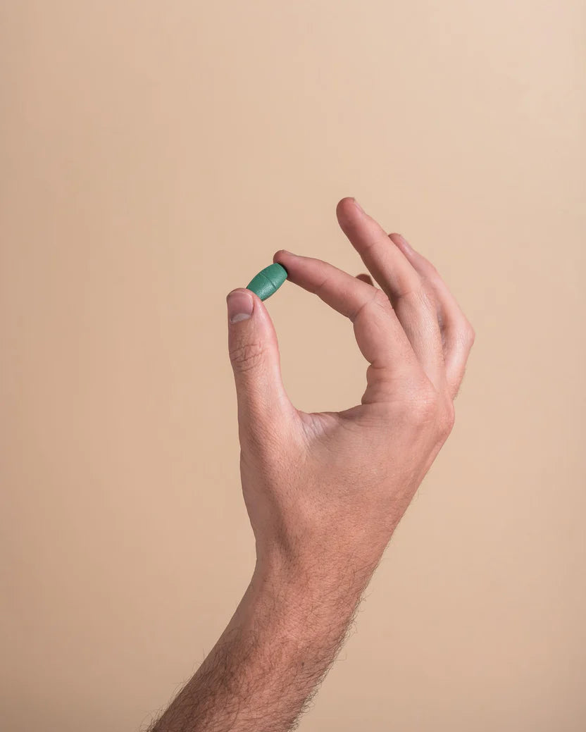 Hand holding a green pill against a beige background