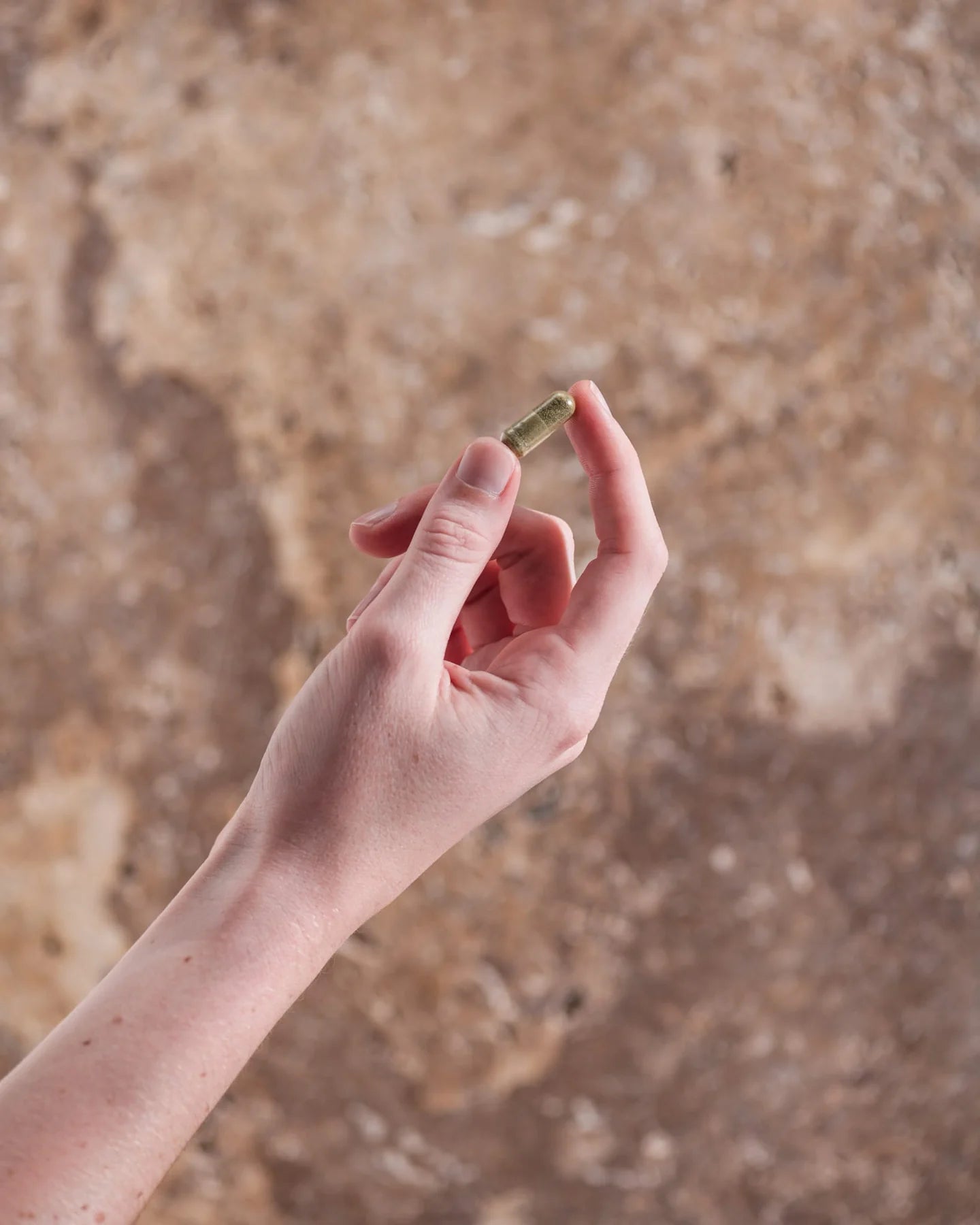 Hand holding a small cylindrical object against a textured brown background