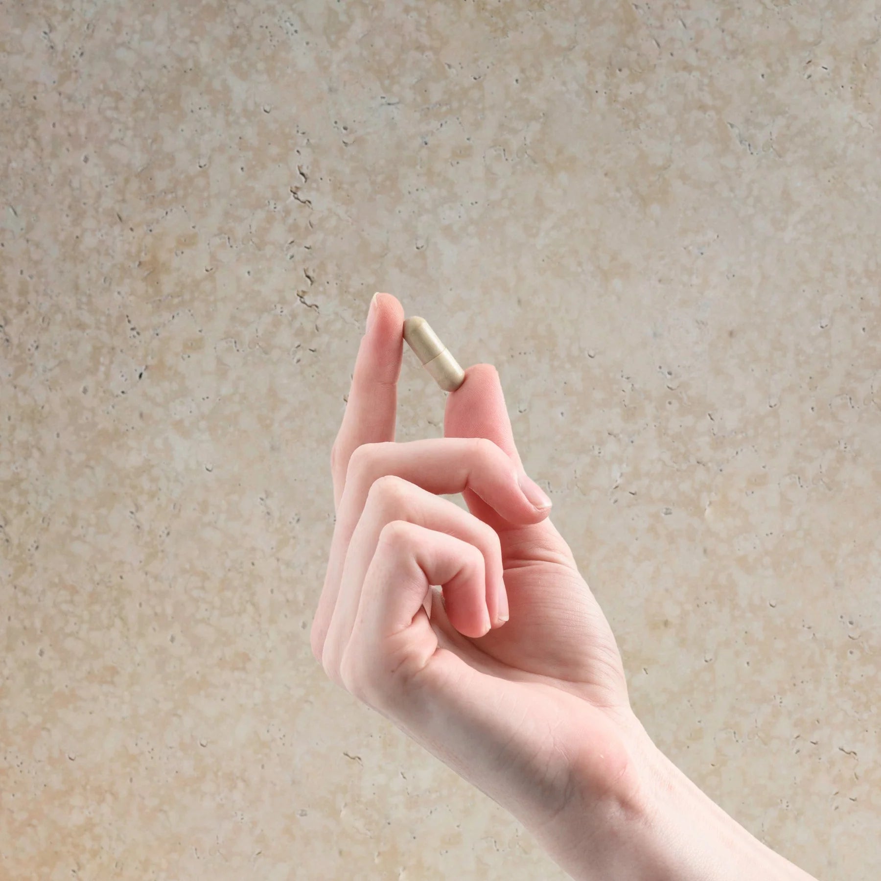 Hand holding a small beige object against a textured background