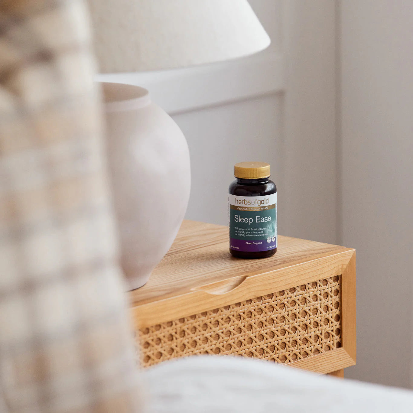 Herbal Gold Sleep Ease bottle on a wooden nightstand beside a lamp.