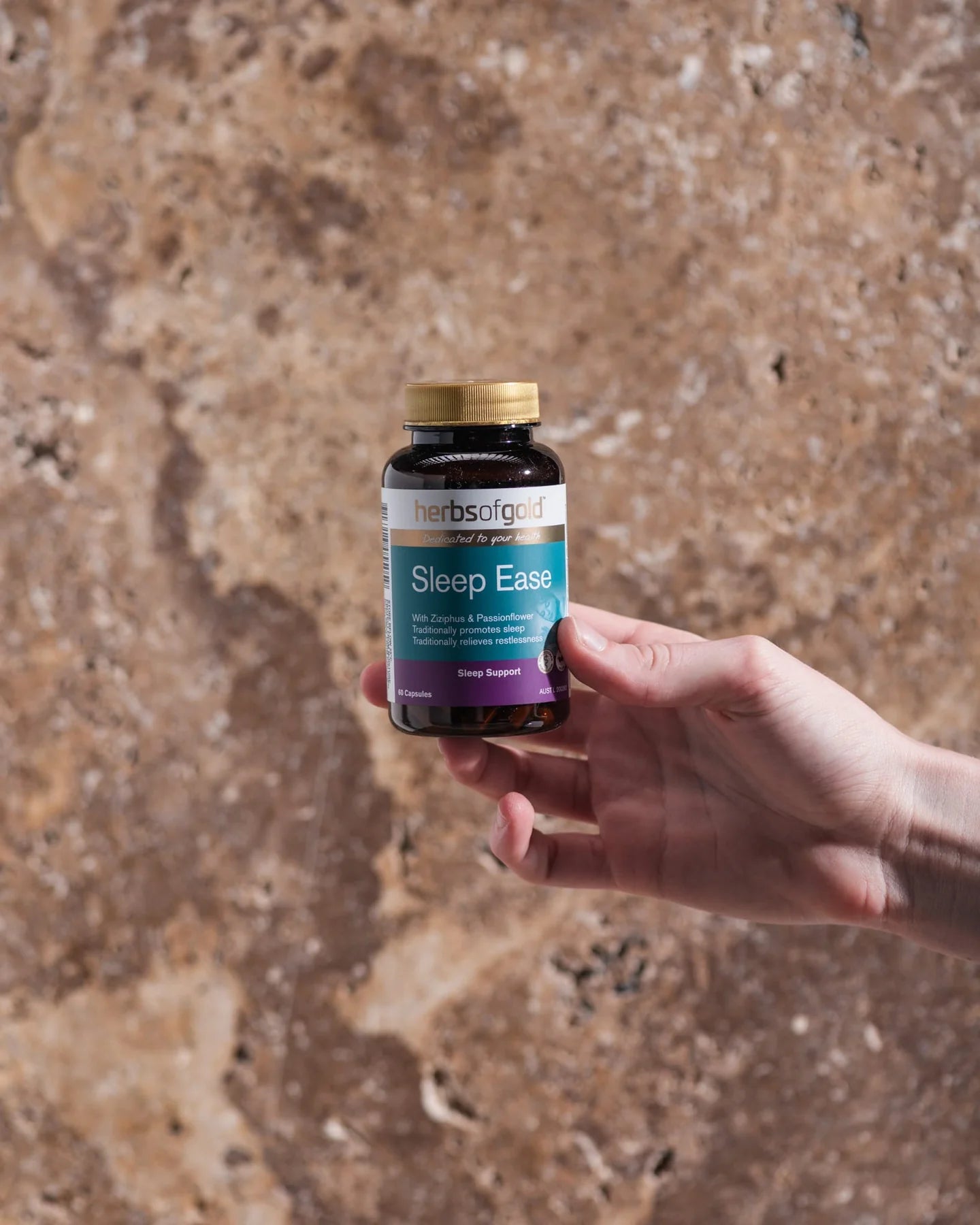 Hand holding a bottle of 'Sleep Ease' supplement against a textured brown background.