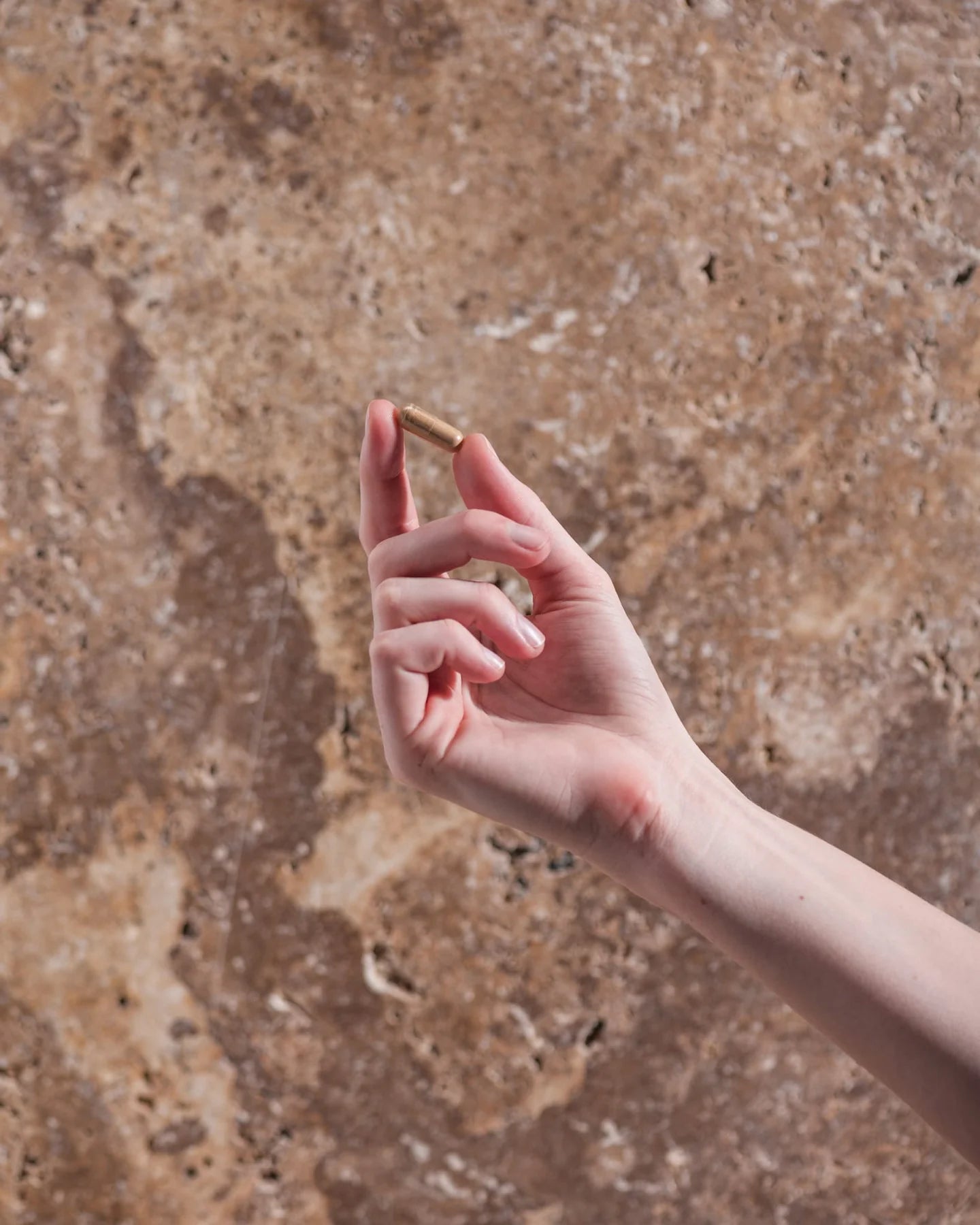 Hand holding a small object against a textured brown background