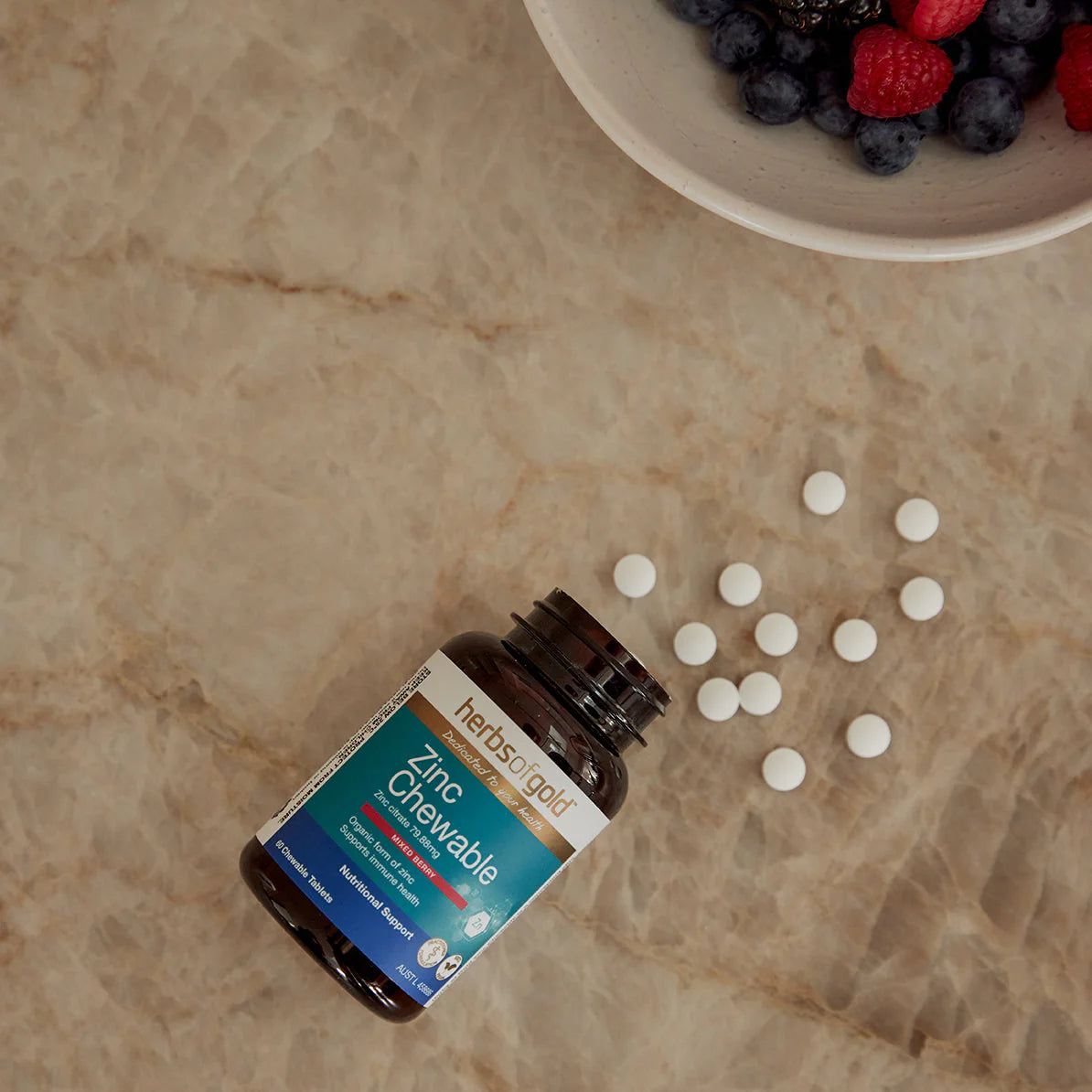 Herbs of Gold Zinc Chewable supplement bottle with scattered tablets on a marble surface.
