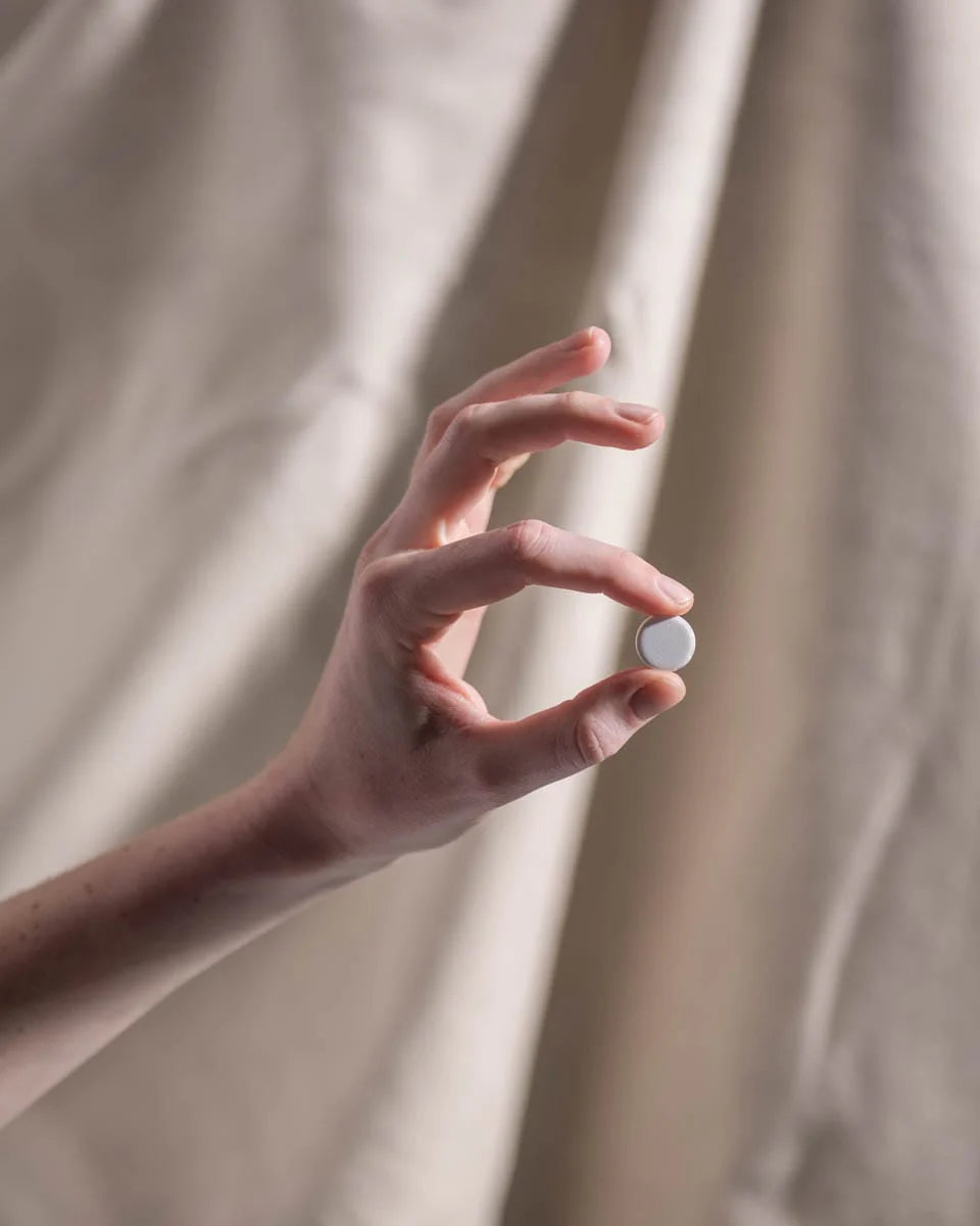 Hand holding a small white object against a beige curtain background