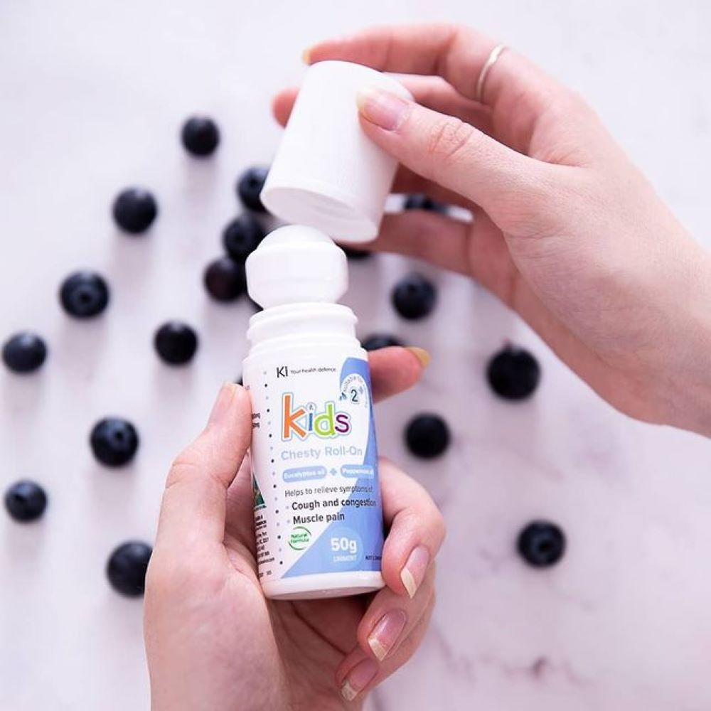 Two hands holding a bottle labeled 'Kids' with blueberries in the background.