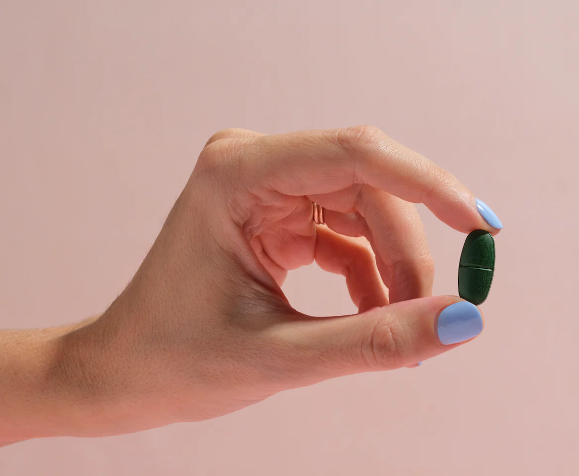 Hand holding a green MitoMag supplement capsule against a soft pink background – available at Nourishing Apothecary.