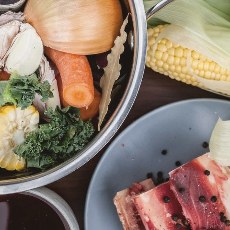 Pot of bone broth ingredients with vegetables, beef bones and fresh corn