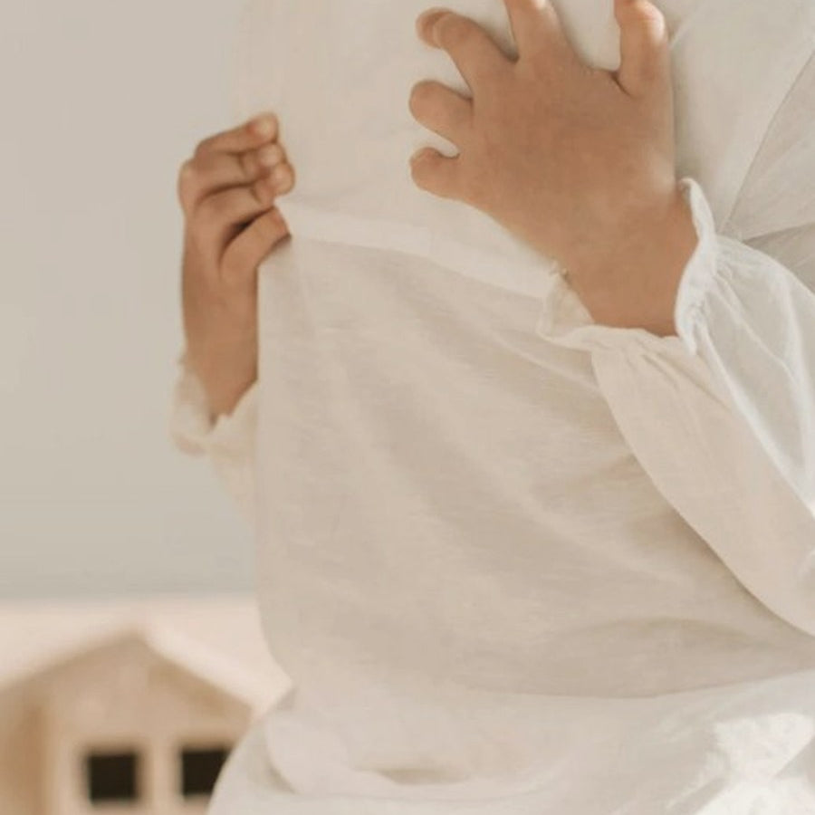 Parent in white linen holding a young child, gentle and warm