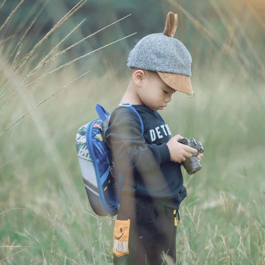 Young child with backpack and camera exploring tall grass at sunset
