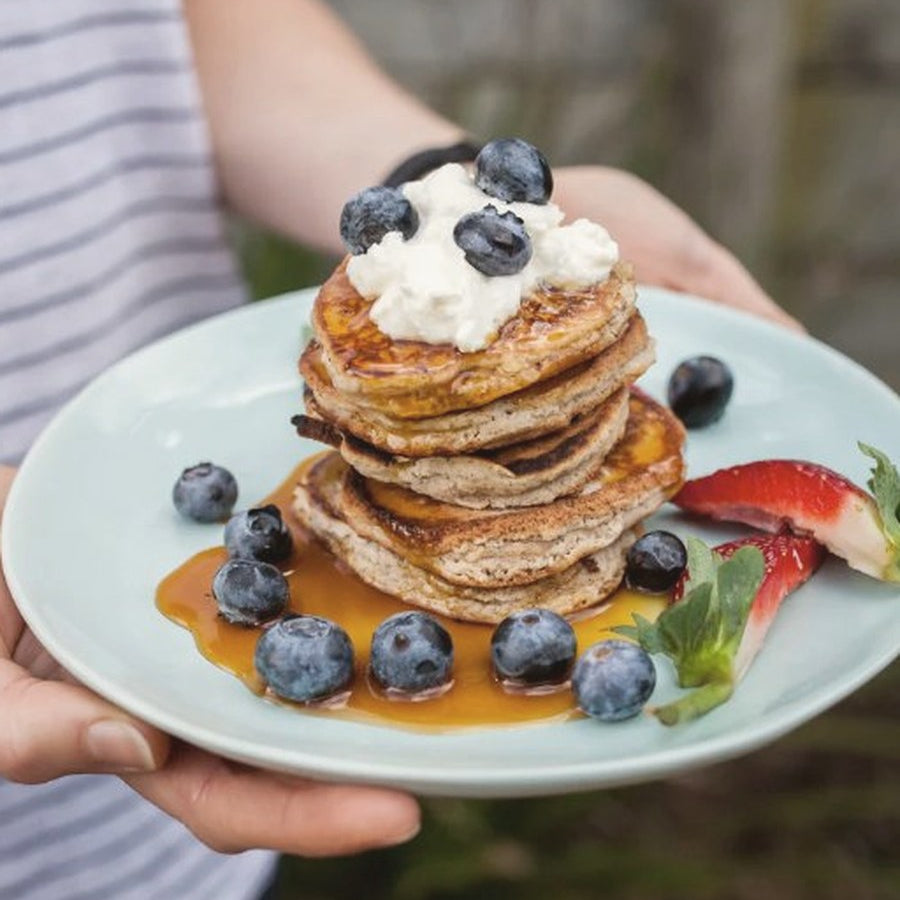 Stack of coconut pancakes topped with blueberries, ricotta and maple syrup
