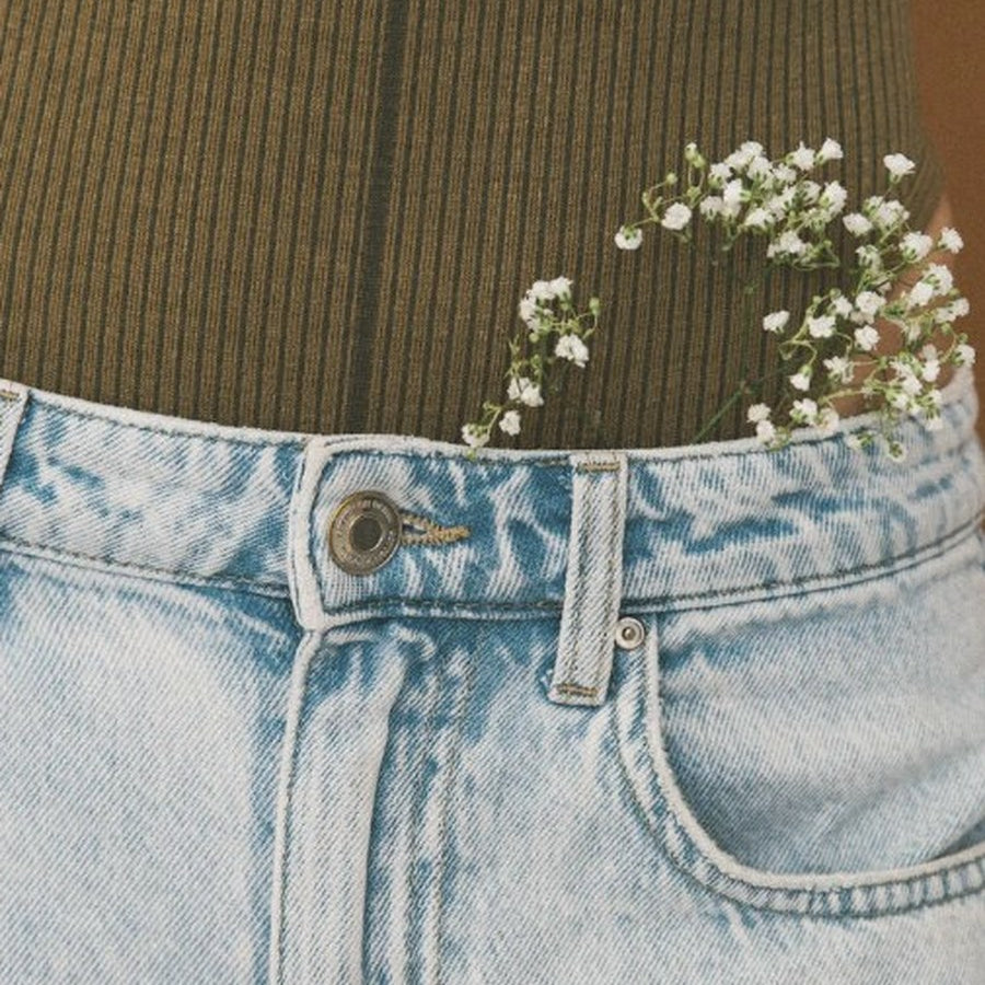 Woman in olive green top and jeans with white baby's breath flowers tucked into her pocket