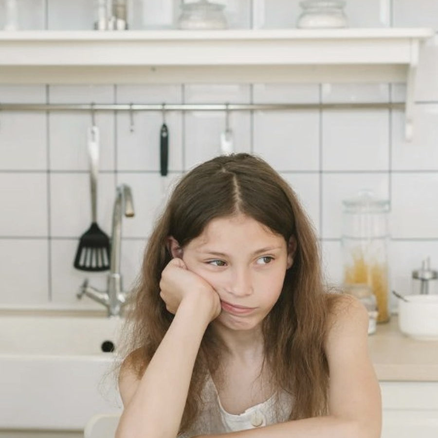 Young girl resting her chin on her hand, looking at a plate of food