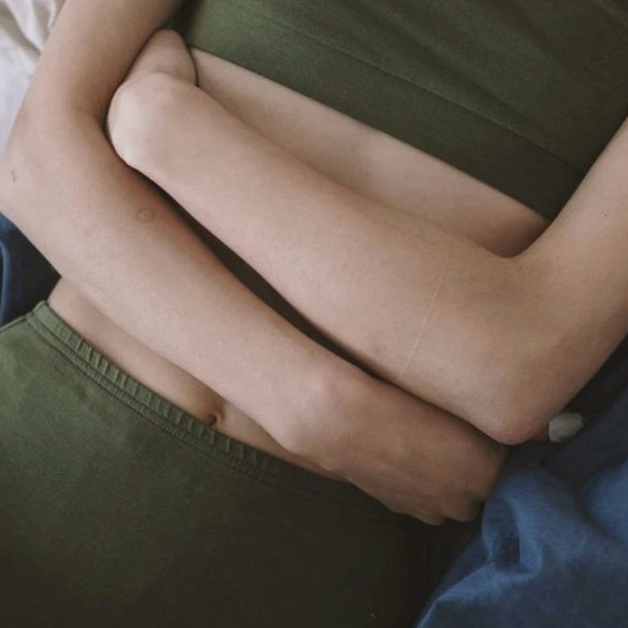 Woman in green crop top and shorts with hands resting on her stomach