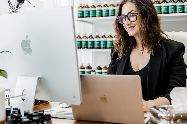 Woman sitting at a desk with a laptop, surrounded by bottles on shelves.