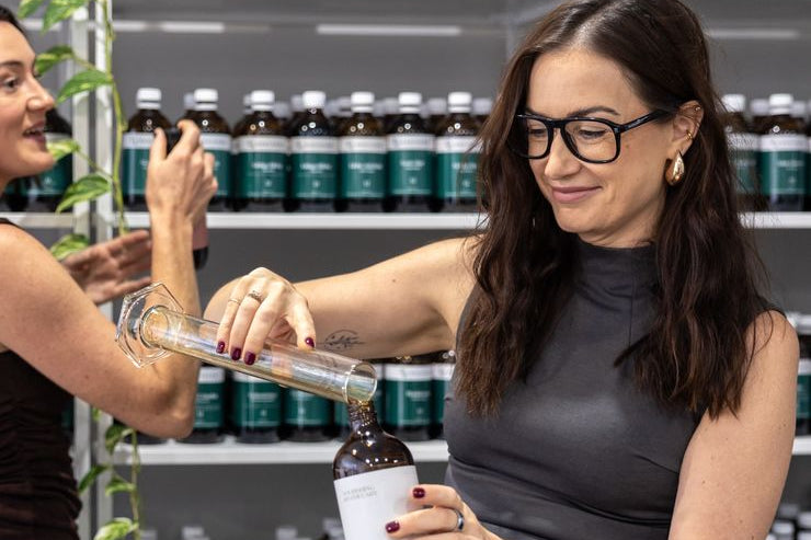 Two women examining a bottle of a product in a store with shelves of similar bottles.