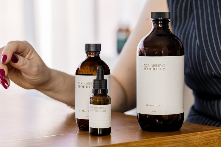 Three bottles of Nourishing Apothecary products on a wooden surface with a blurred background.