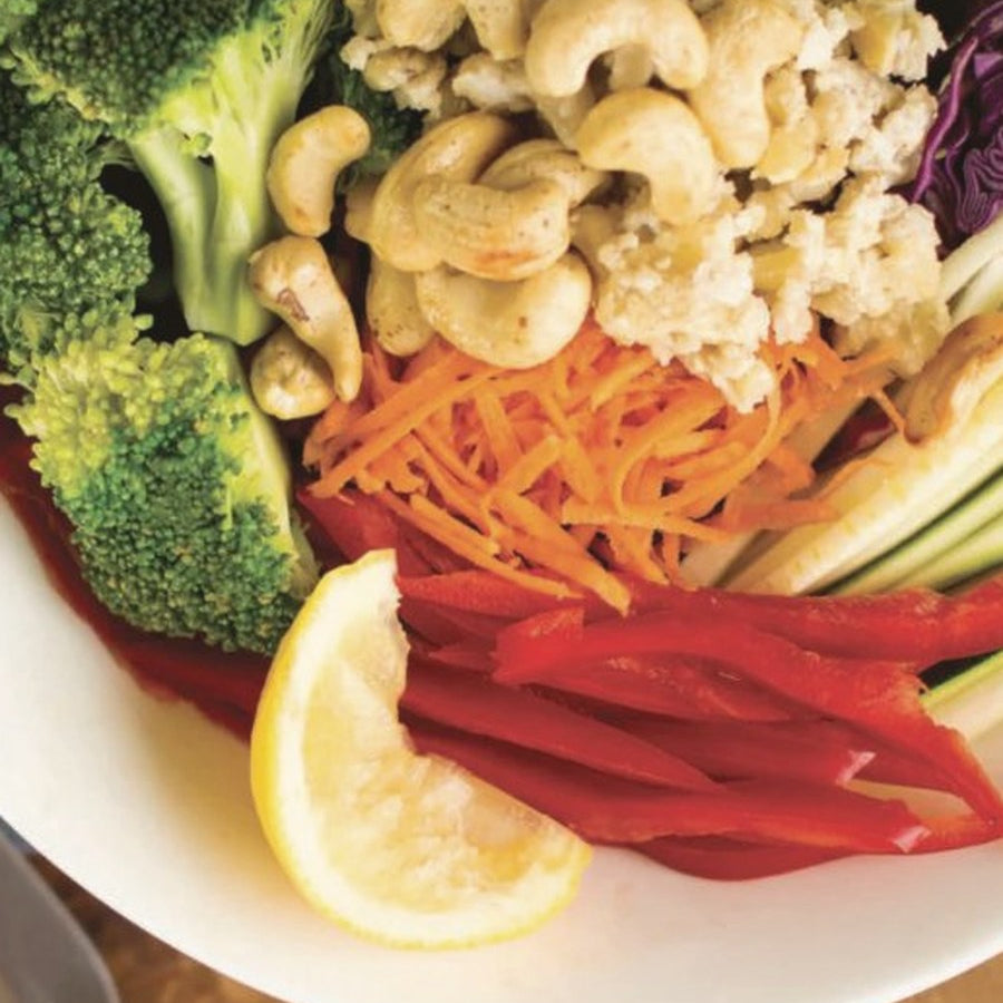 Buddha bowl with broccoli, cashews, carrot, red capsicum, avocado and lemon on a wooden board