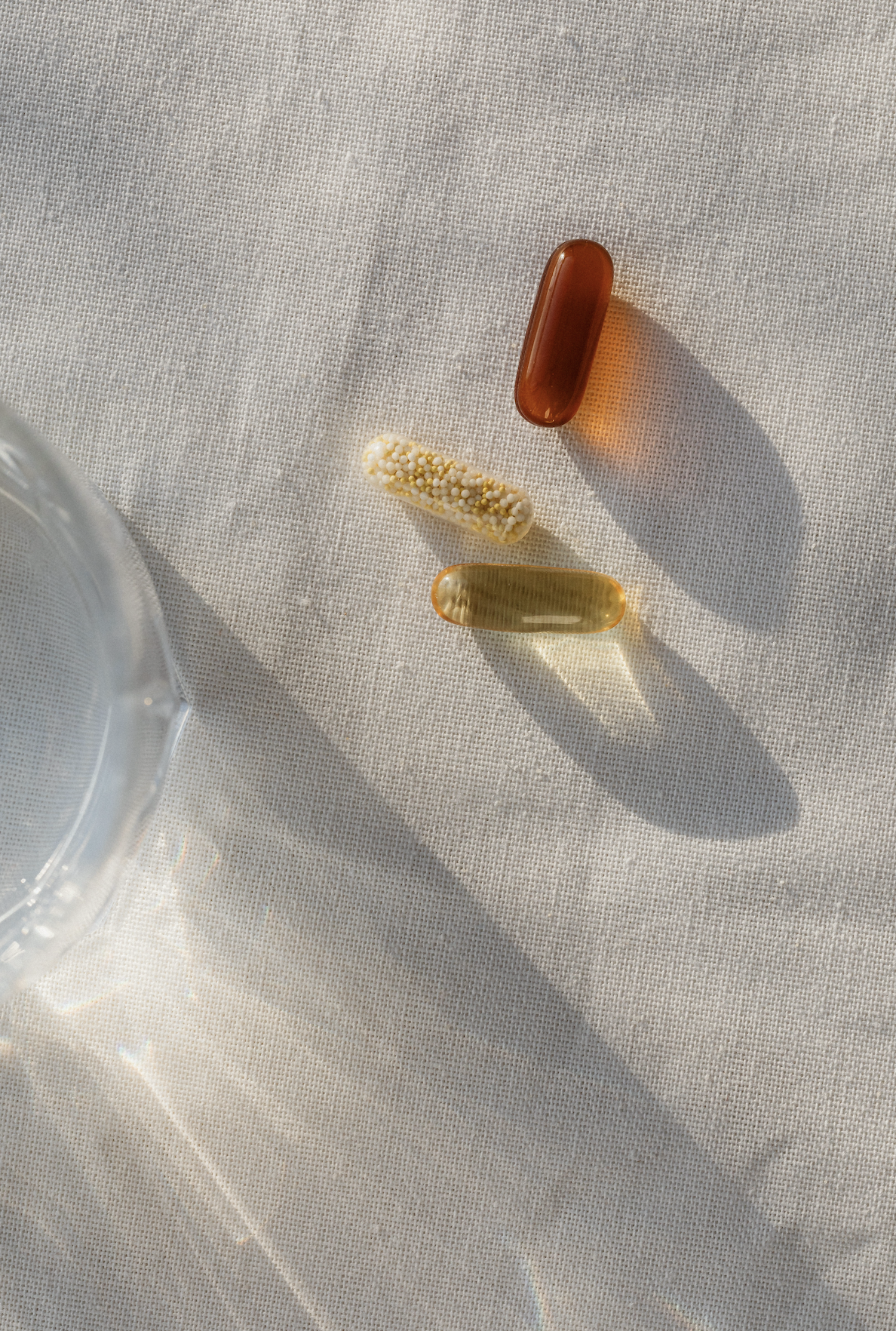 Three dietary supplement capsules (omega-3, herbal, and multivitamin) on a linen surface in natural sunlight, representing natural menopause support.