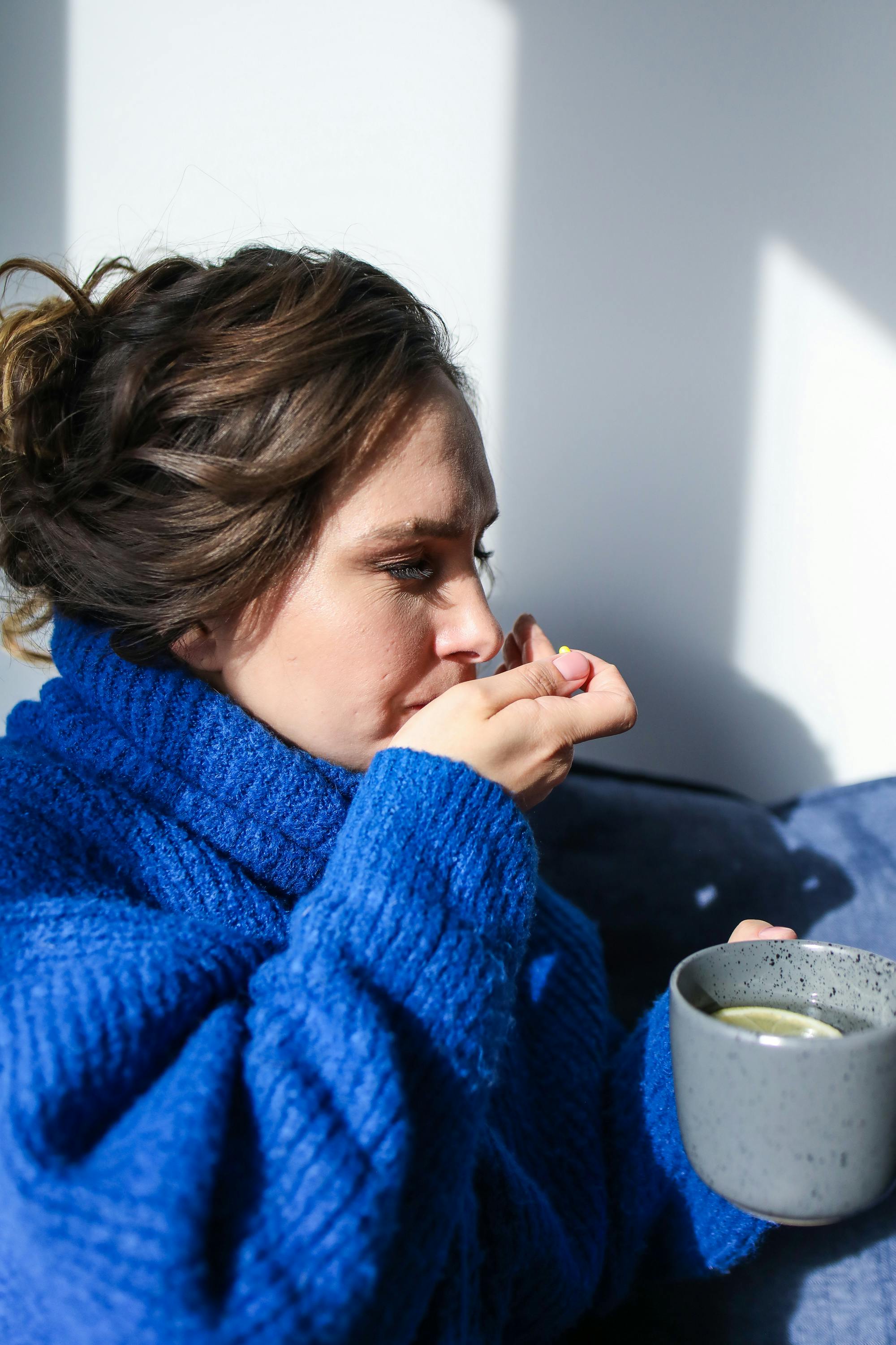 Woman holding a warm drink and taking a supplement capsule