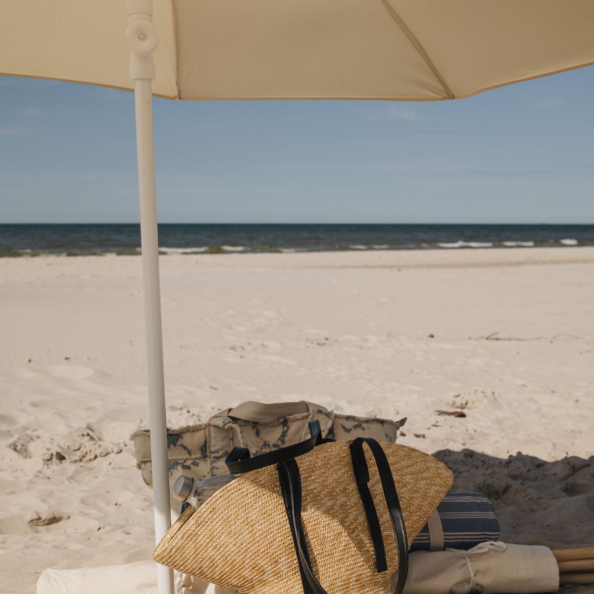 Calm beach scene with umbrella and woven bag, representing rest, balance, and holistic wellness.