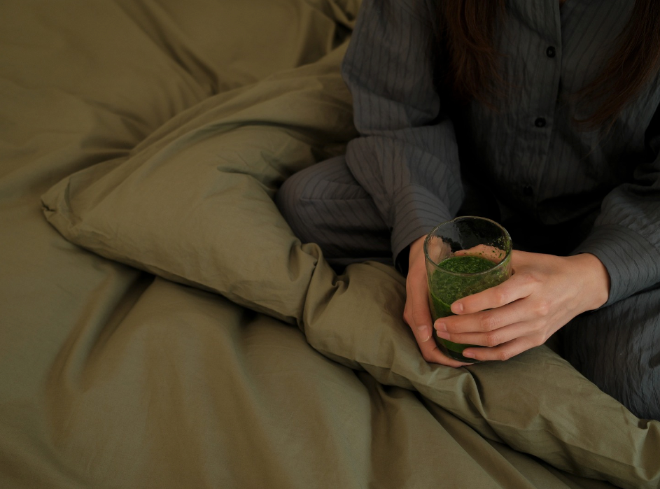 Fatigued woman starting her day in bed with a comforting cup of supplements to support energy and balance.