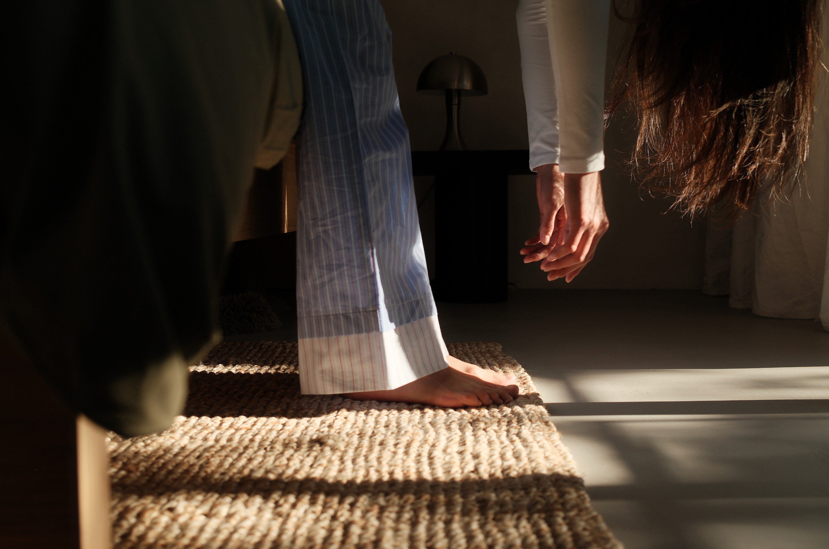 A woman gently stretching on a woven rug in morning light, symbolising self-care and natural wellness practices for menopause support.