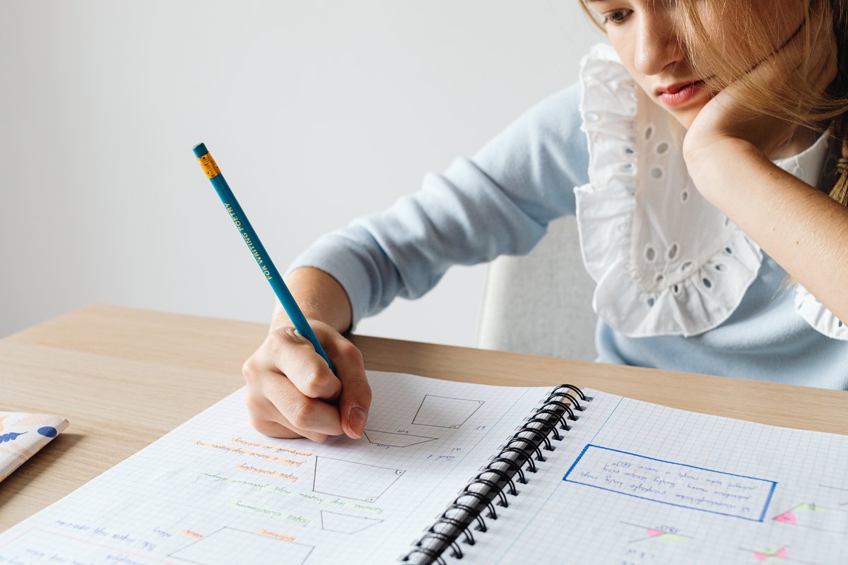 Child resting their chin on one hand while doing homework in a notebook