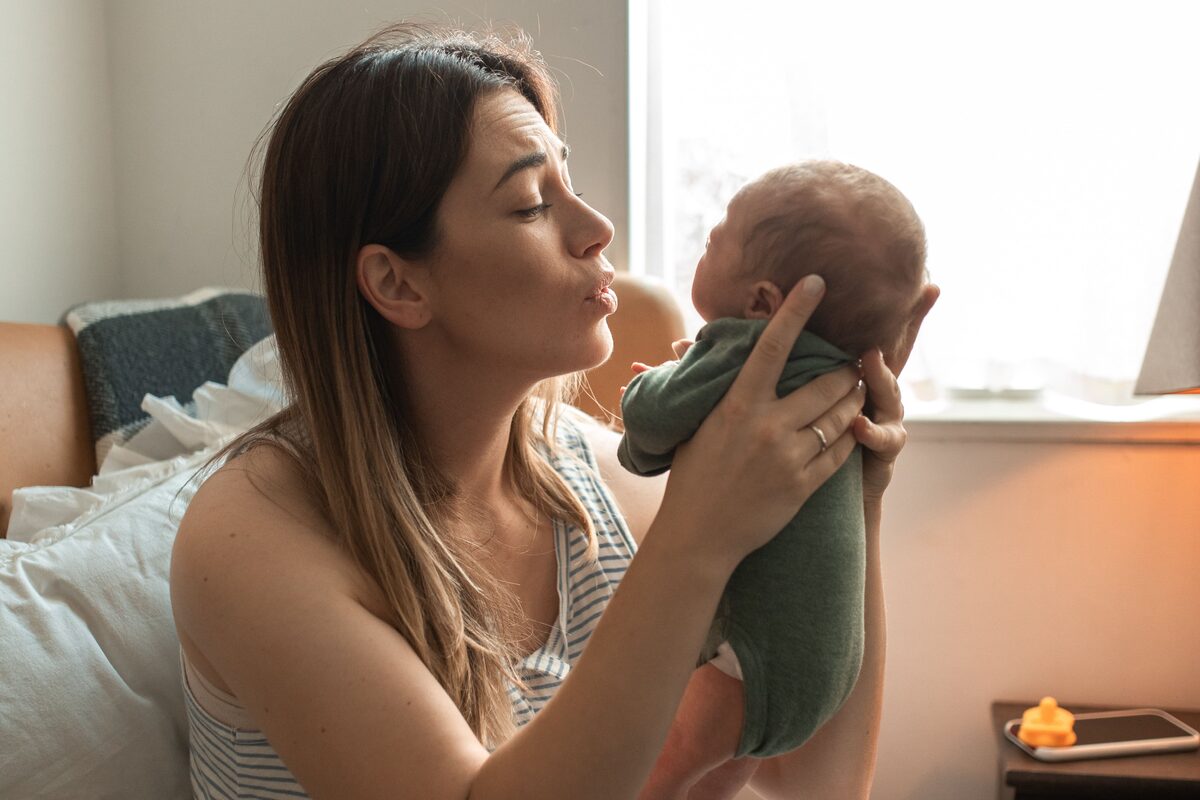 Mother sitting by a window holding her newborn baby in the early postnatal period