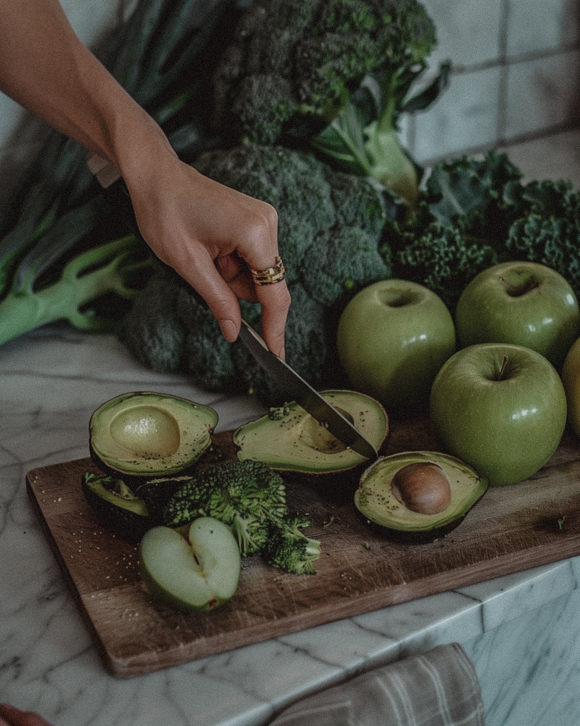 A flat lay of healthy hormone-supporting foods including avocados, leafy greens, seeds, and herbal supplements, styled naturally on a wooden table.