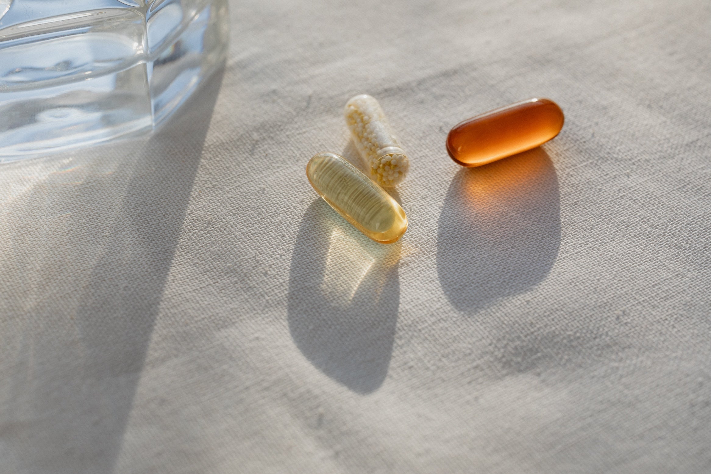 Three natural supplement capsules on fabric in soft morning light, symbolising daily wellness support.