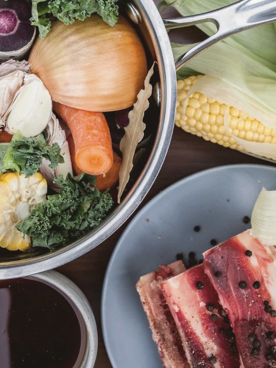 Pot of bone broth ingredients with vegetables, beef bones and fresh corn