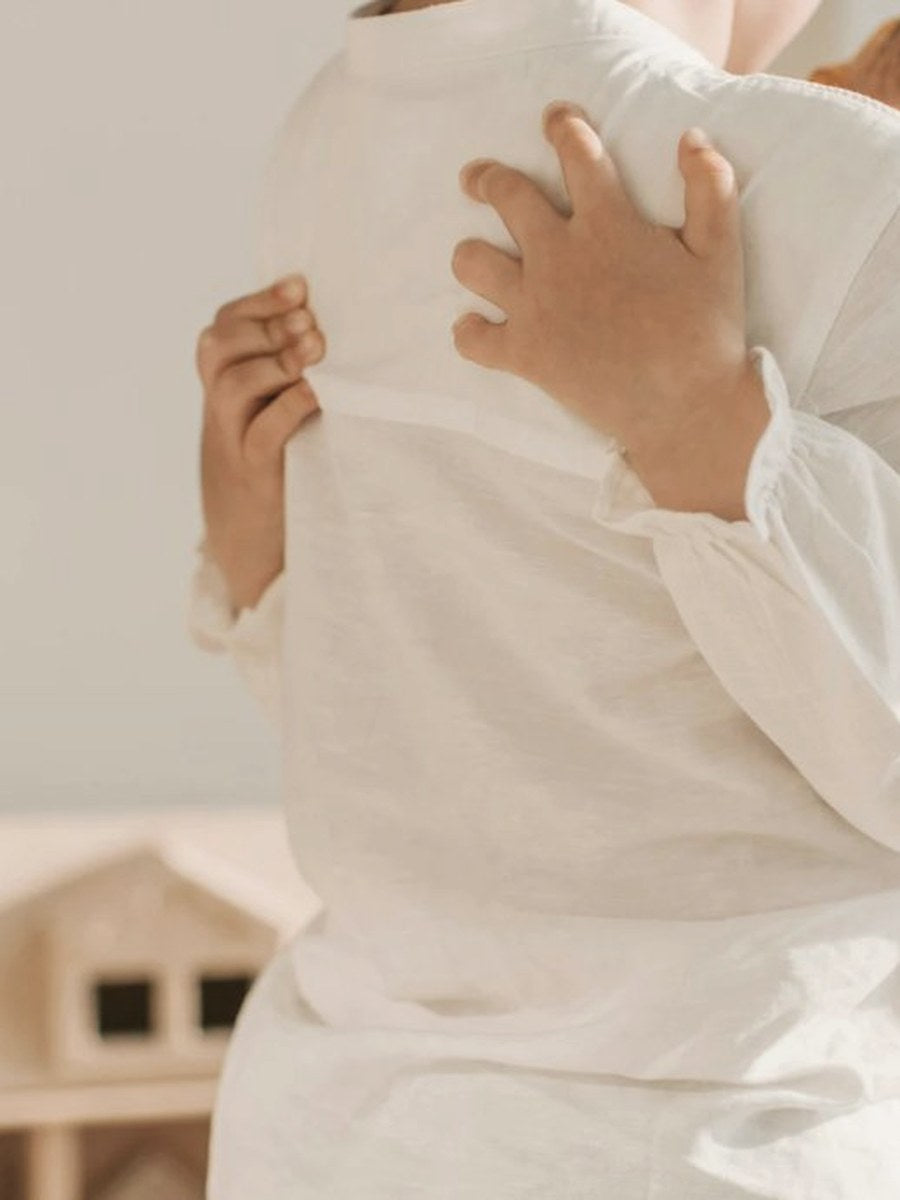 Parent in white linen holding a young child, gentle and warm