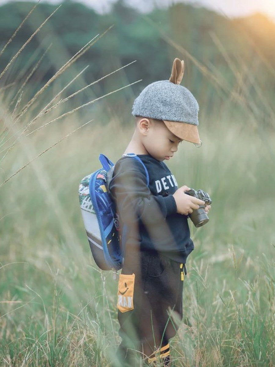 Young child with backpack and camera exploring tall grass at sunset